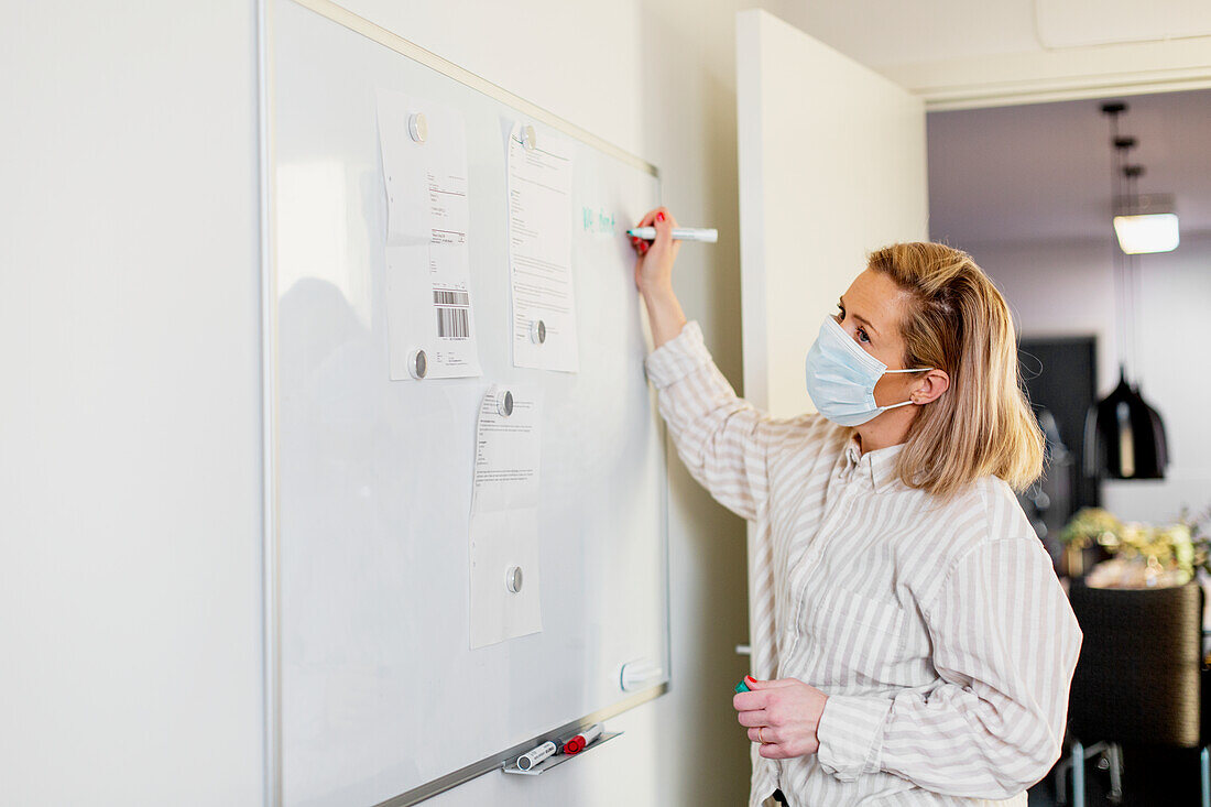 Woman wearing protective face mask writing on whiteboard