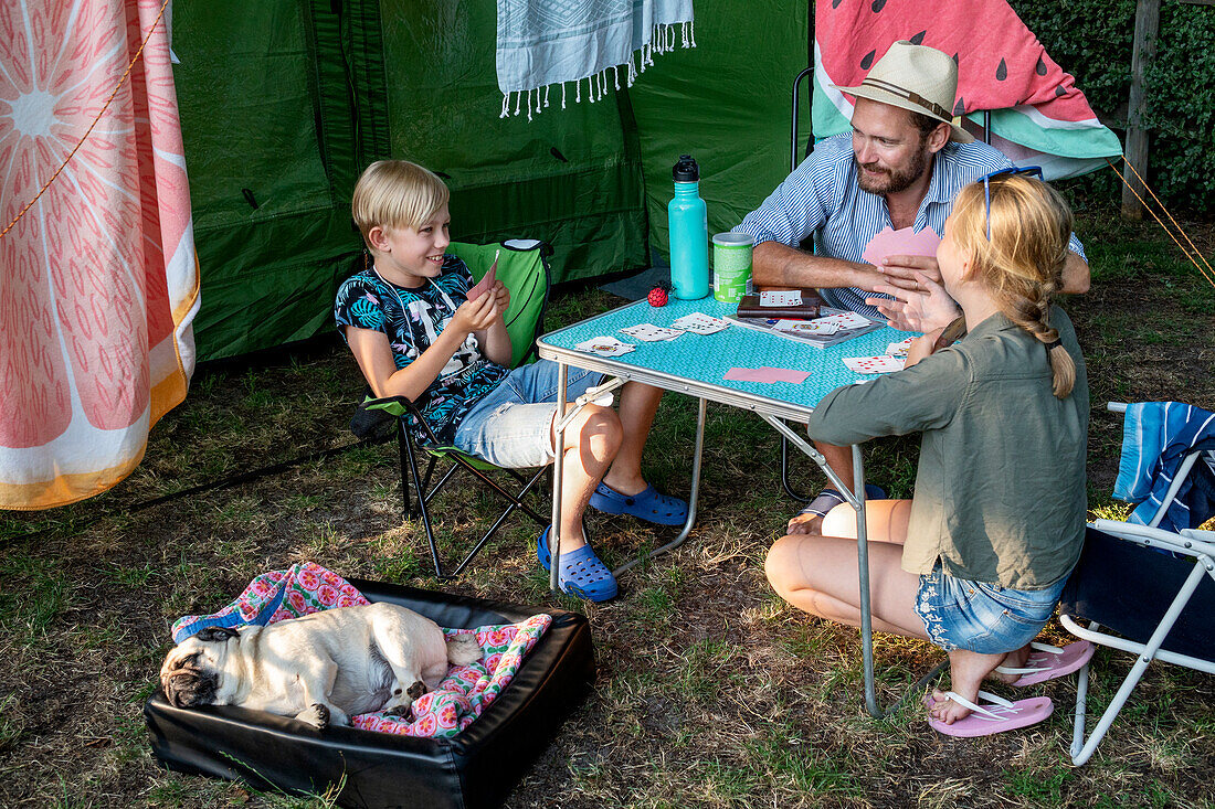 Vater mit Kindern beim Kartenspielen vor dem Zelt