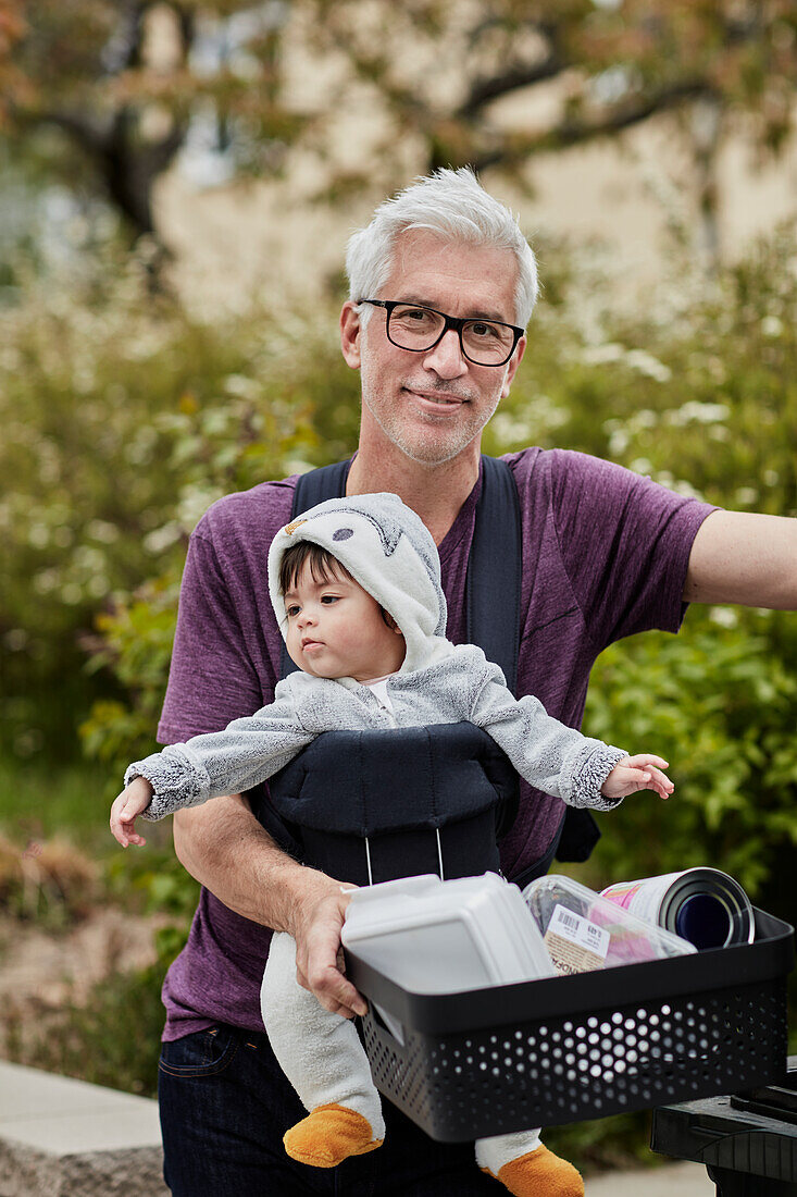Lächelnder reifer Mann mit Baby, das Recycling trägt