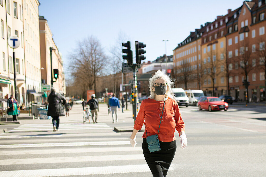 Frau mit Gesichtsmaske beim Überqueren der Straße