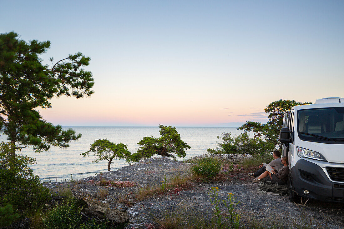 Couple sitting near van and looking at sunset