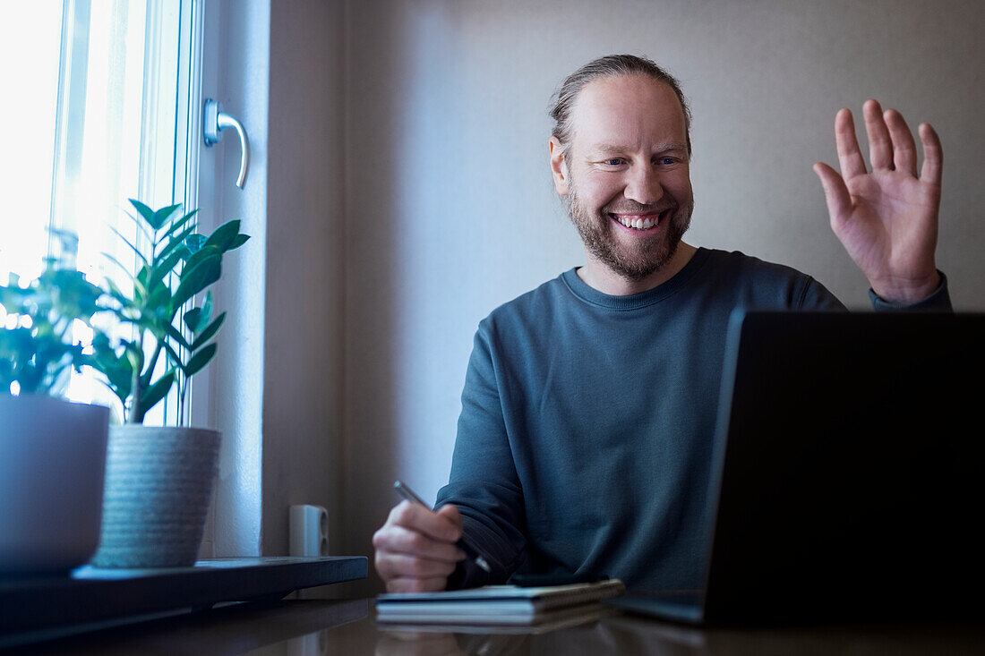 Smiling man doing notes while looking at laptop