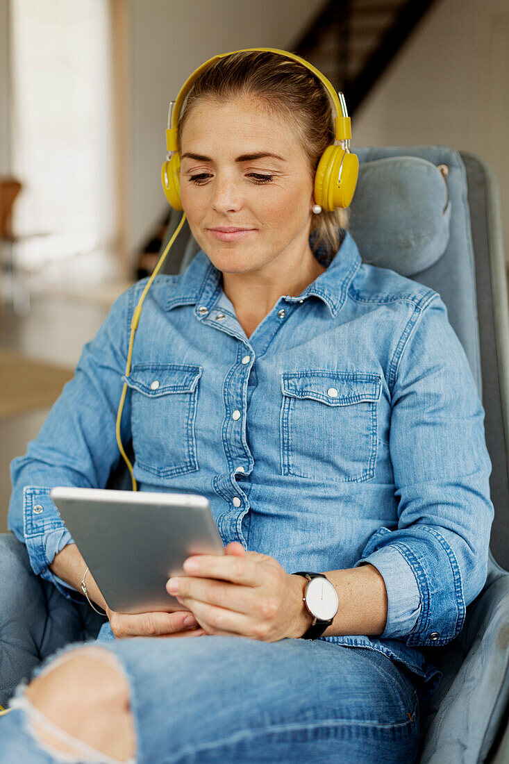 Frau im Sessel sitzend und mit digitalem Tablet