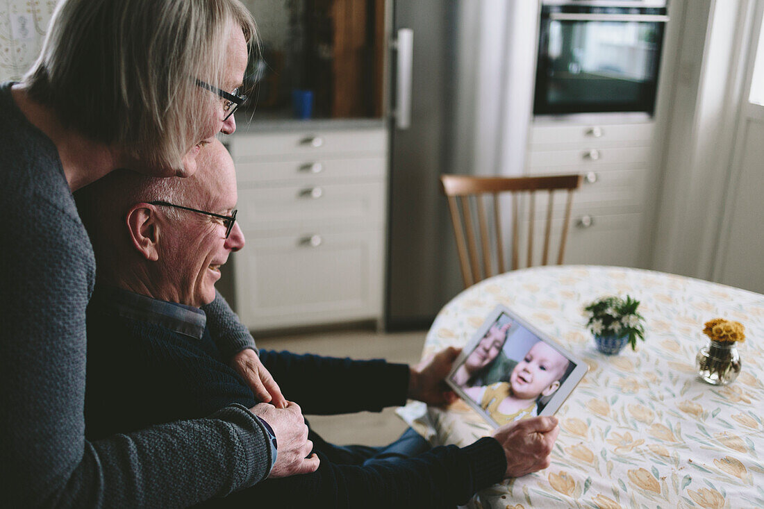 Smiling couple having video chat with baby grandson on tablet