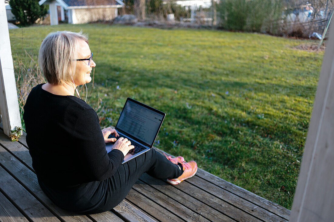 Frau sitzt auf Veranda und arbeitet am Laptop