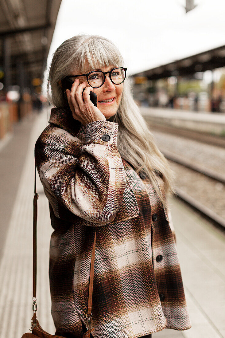 Reife Frau am Telefon auf dem Bahnhof