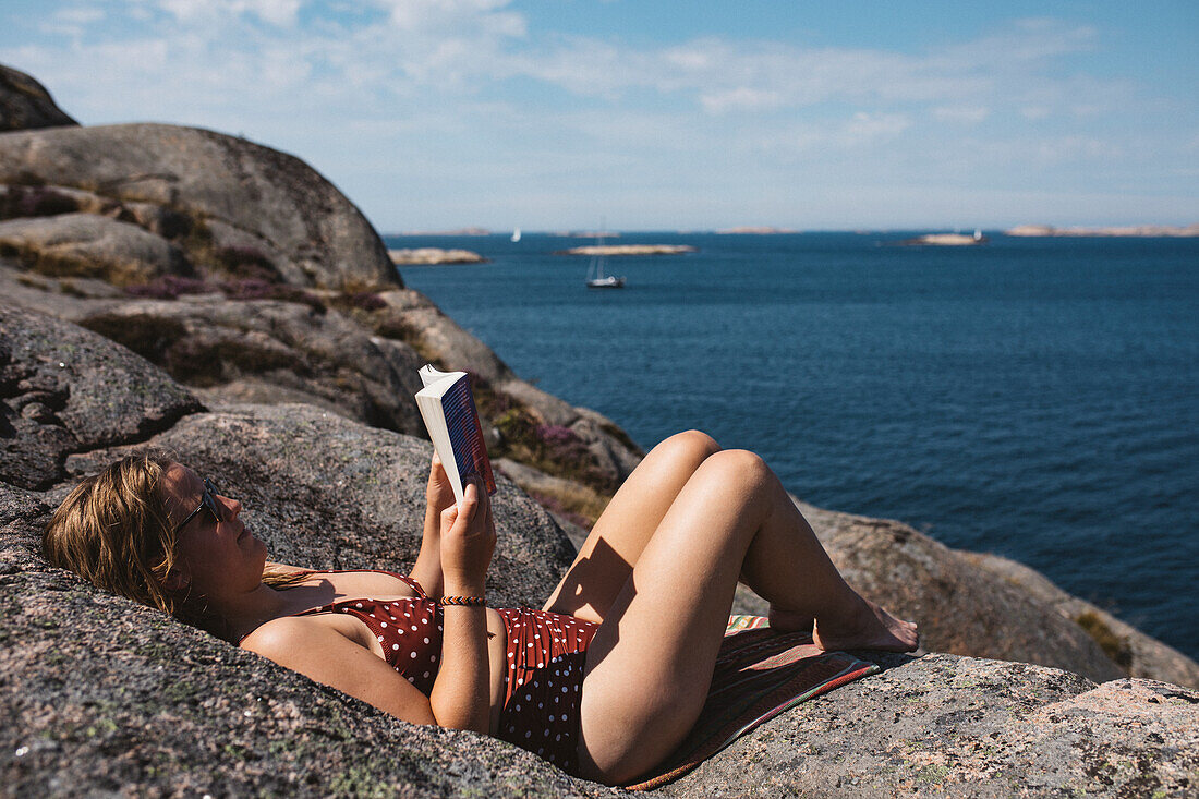 Woman reading book on rocky coast