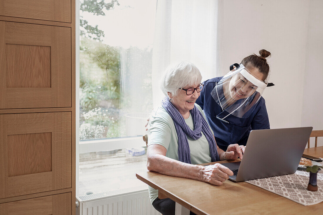 Home carer helping senior woman to use laptop
