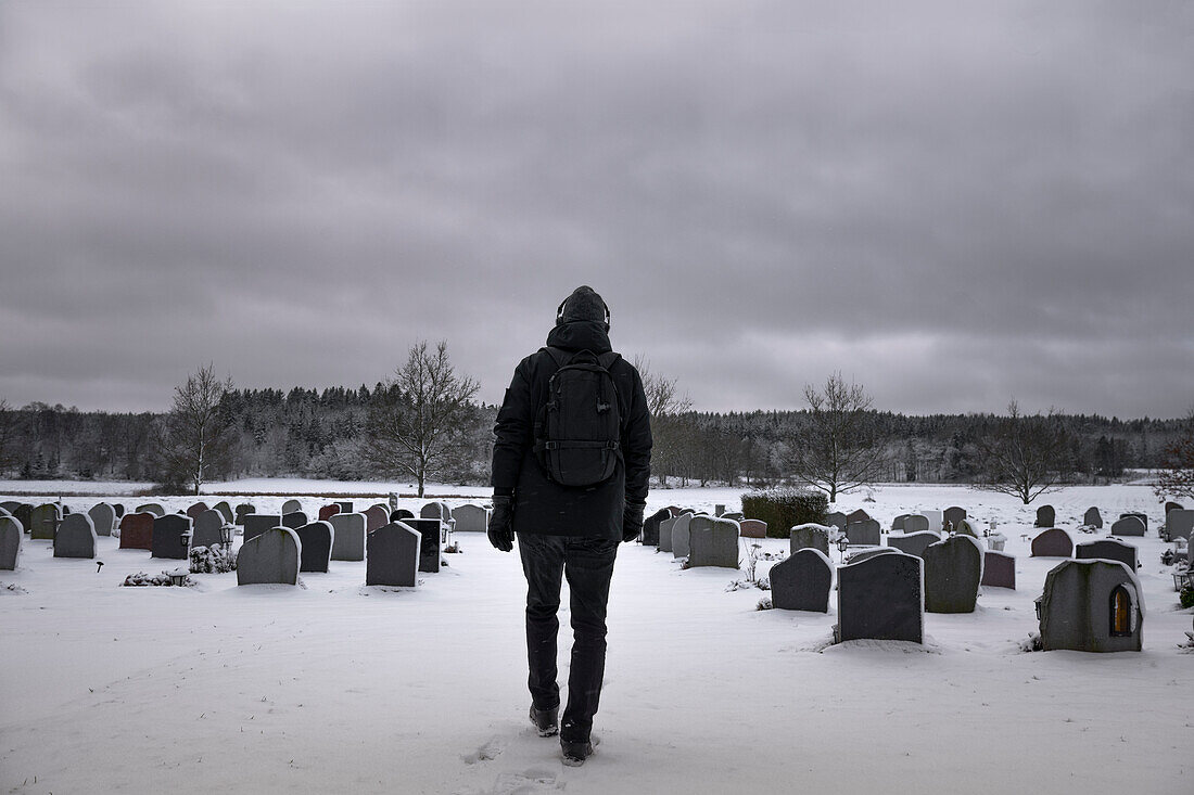 Man walking through snowy cemetery