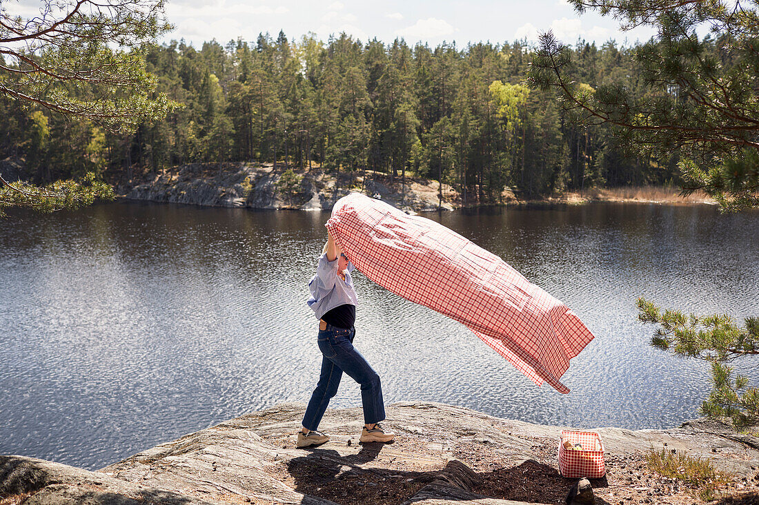 Woman with picnic blanket standing on cliff over lake