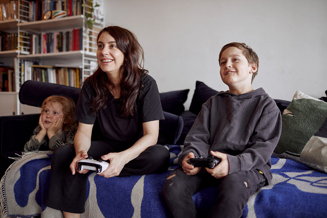 Mother with sons sitting on sofa and playing video games