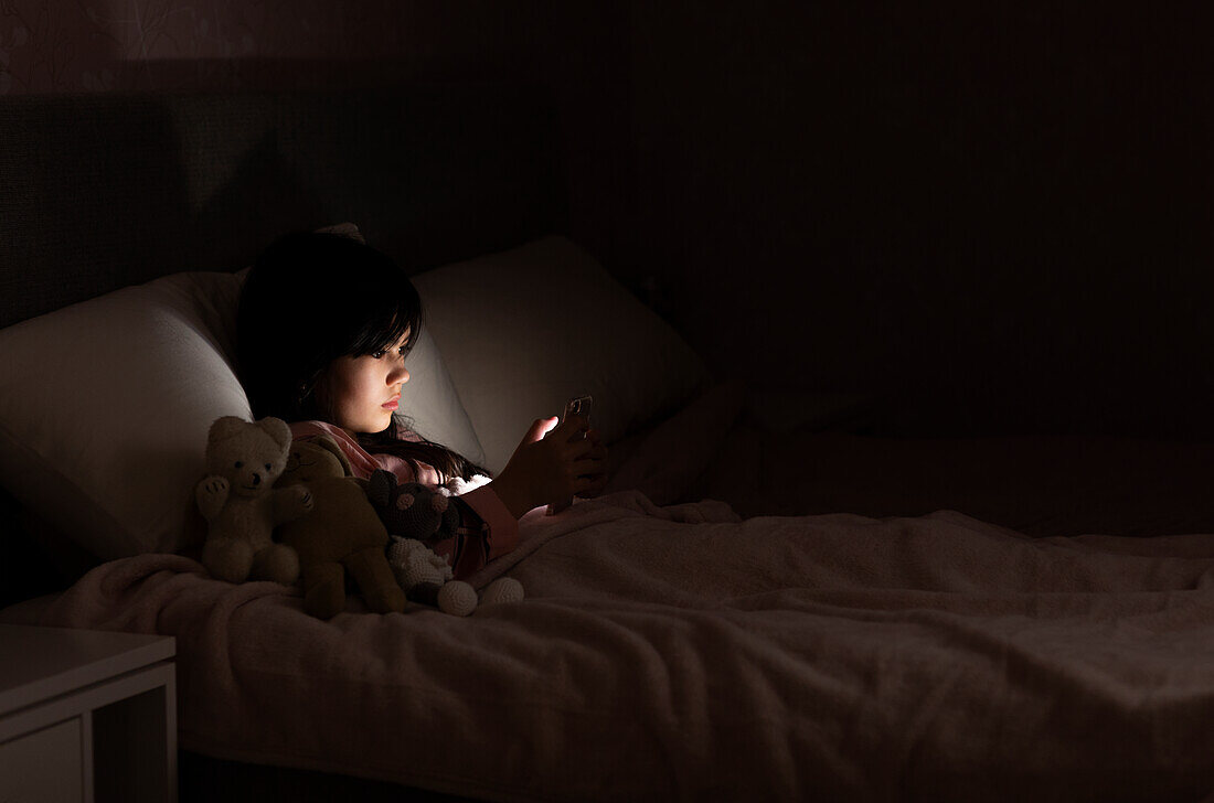Mädchen benutzt Handy im Bett