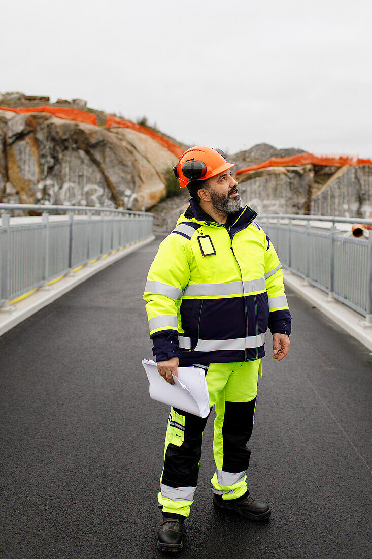 Male engineer in reflecting clothing standing on bridge