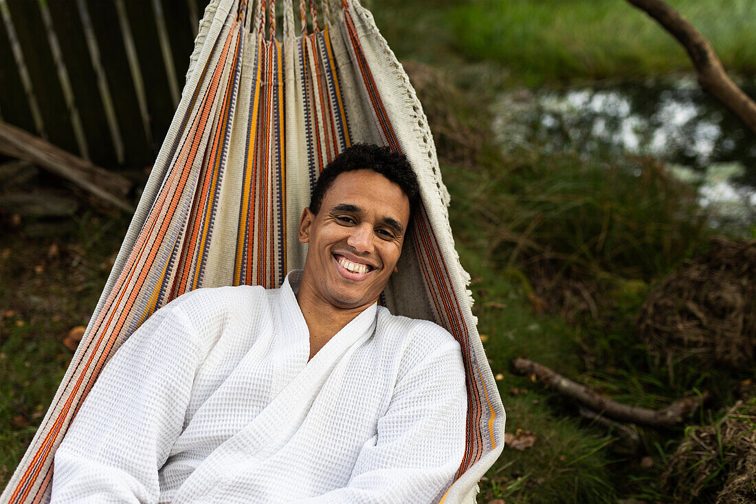Lächelnder junger Mann im Bademantel entspannt sich in der Hängematte