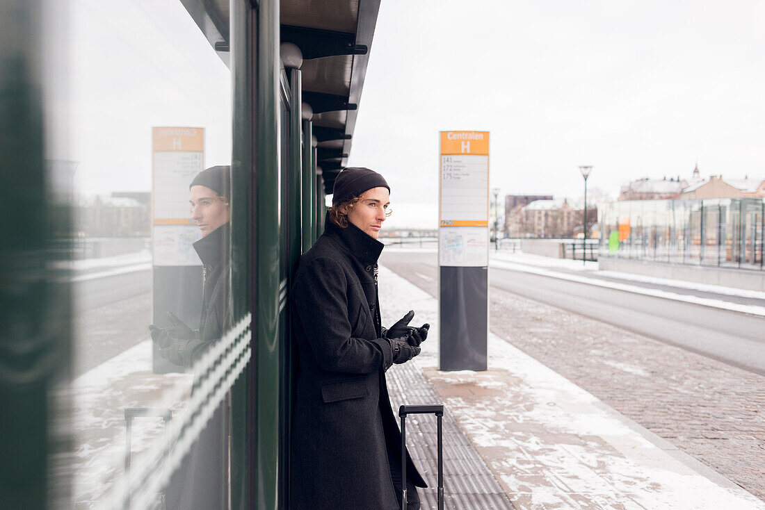 Junger Mann wartet an einer Bushaltestelle im Winter
