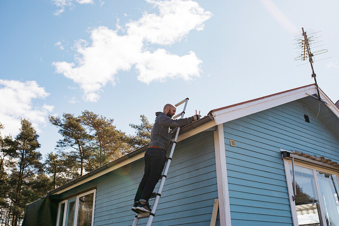 Man cleaning gutter on cottage