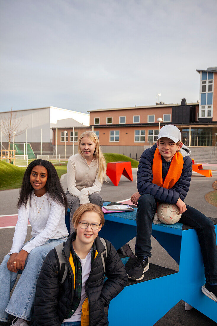 Portrait of teenage friends sitting in front of school