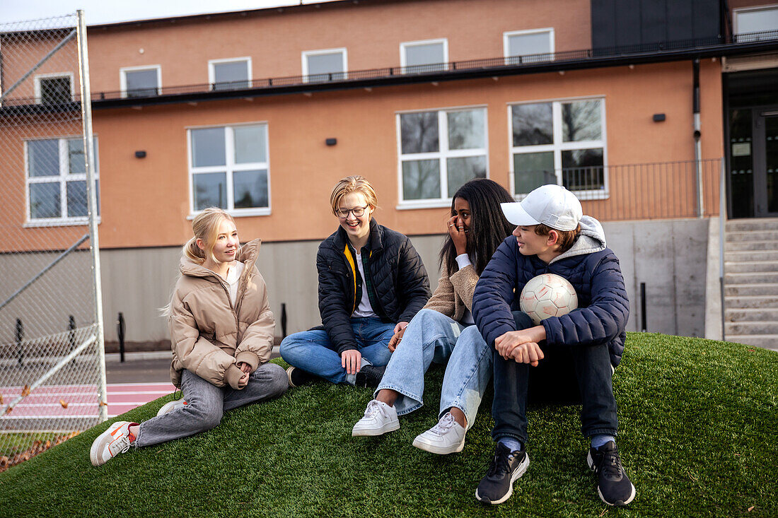 Teenage friends sitting on lawn in front of school