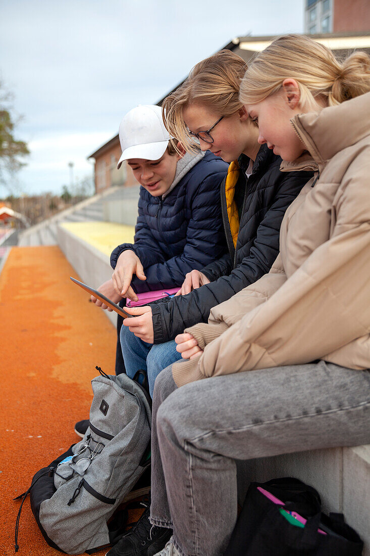 School friends sitting in front of school and using laptop