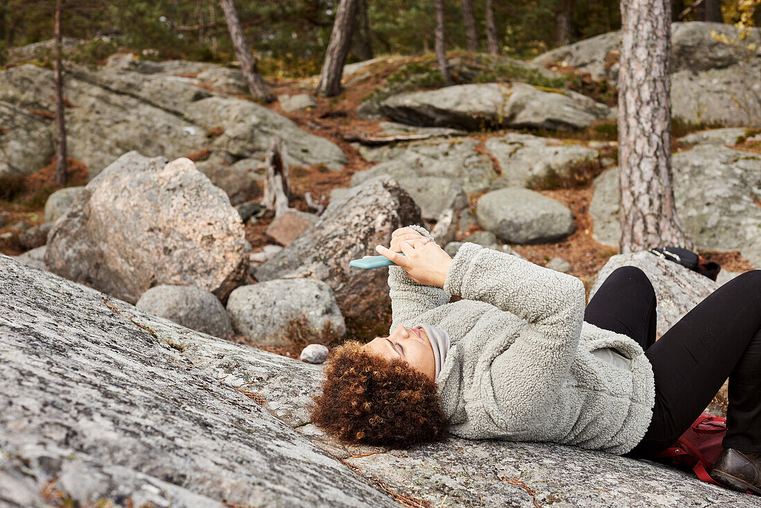 Woman lying on rocks and using smart phone