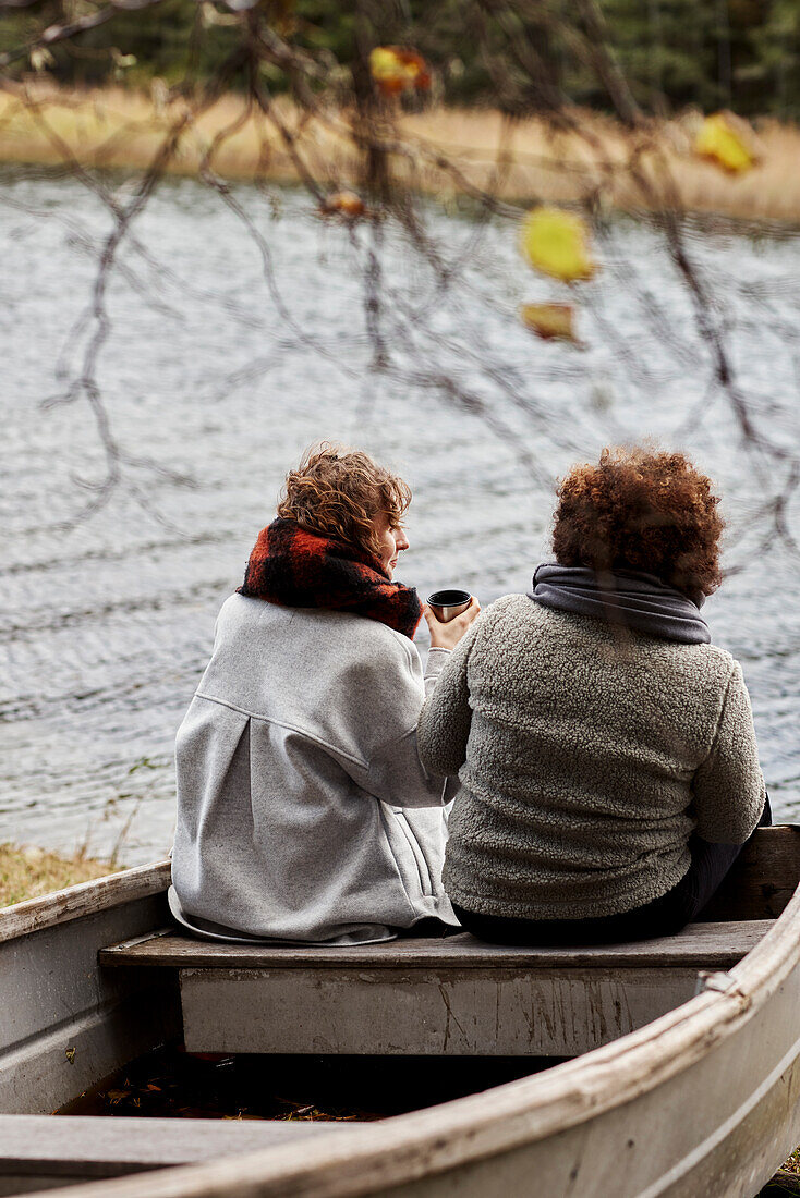 Female friends sitting on old boat by lake