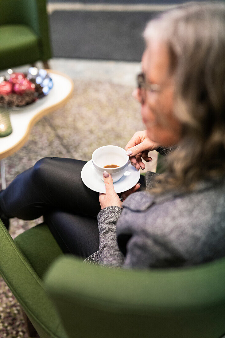 Ältere Frau sitzt im Sessel und trinkt Kaffee