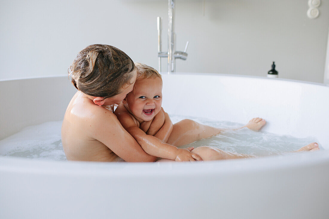 Smiling siblings hugging in bathtub