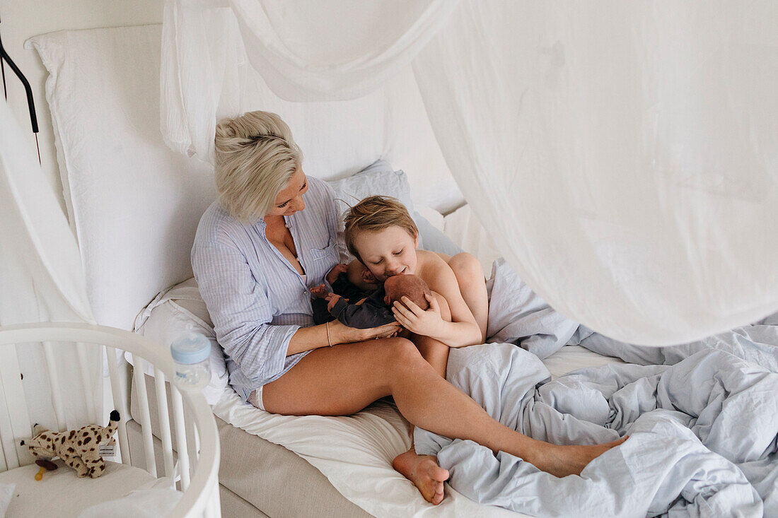 Mutter und Sohn liegen im Bett mit neugeborenem Baby