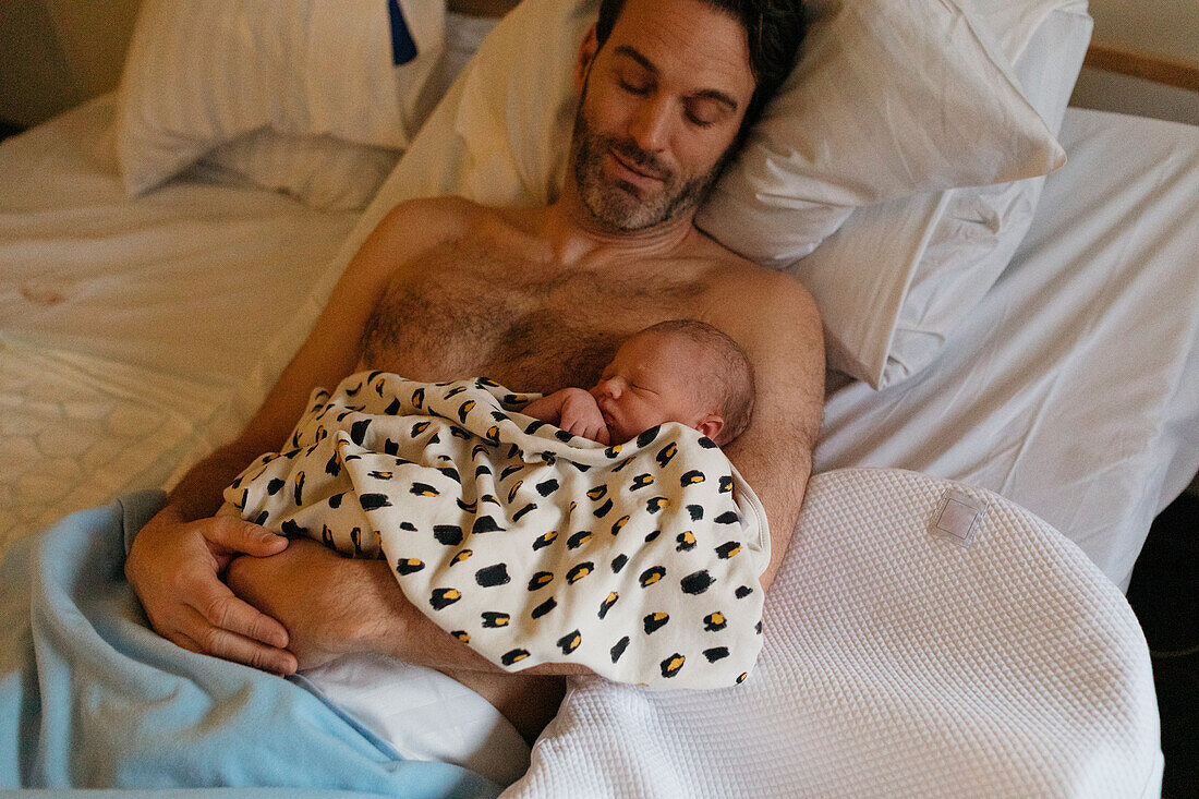 Vater liegt mit neugeborenem Kind im Bett