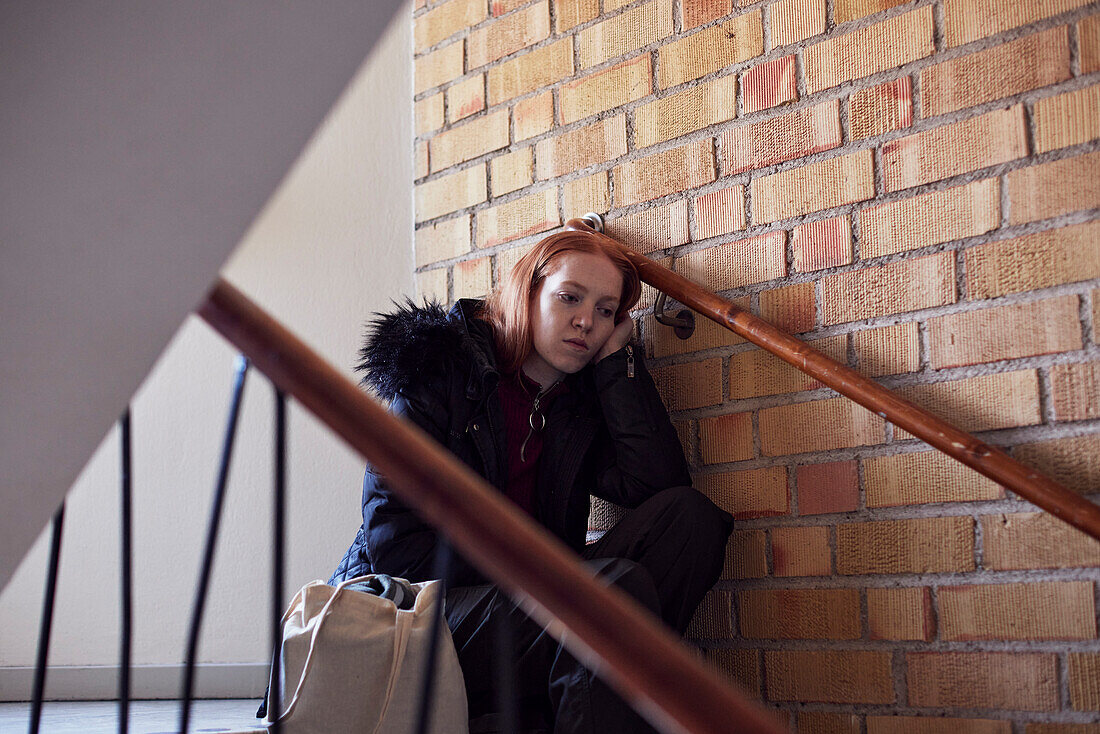 Junge Frau sitzt auf einer Treppe und lehnt sich an die Wand