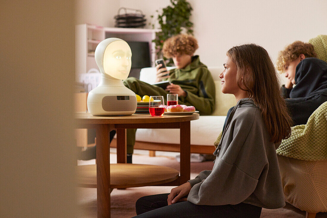 Siblings sitting in living room and using robotic voice assistant