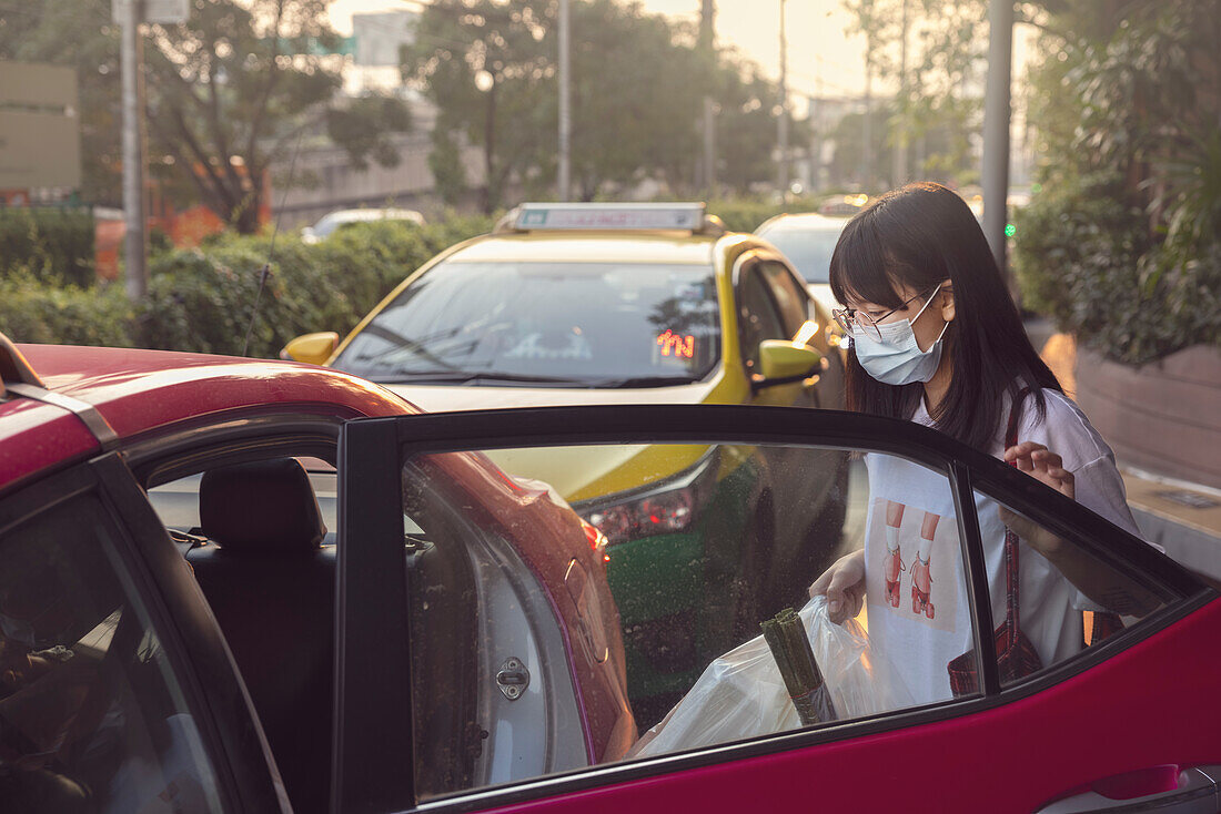 Frau mit Gesichtsschutzmaske steigt in ein Taxi