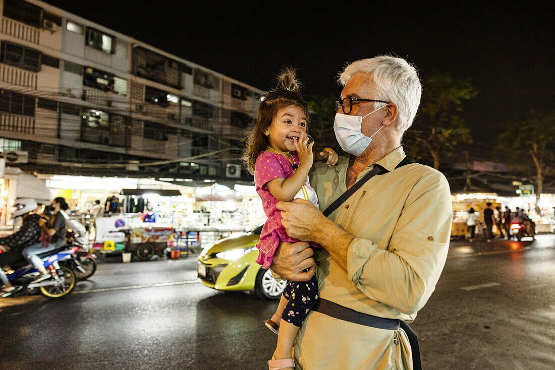 Grandfather holding granddaughter in street at night