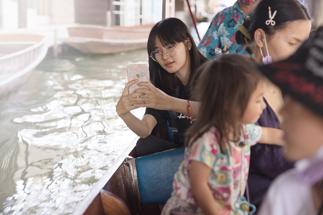 Junge Frau sitzt in einem Boot und macht Fotos mit ihrem Smartphone