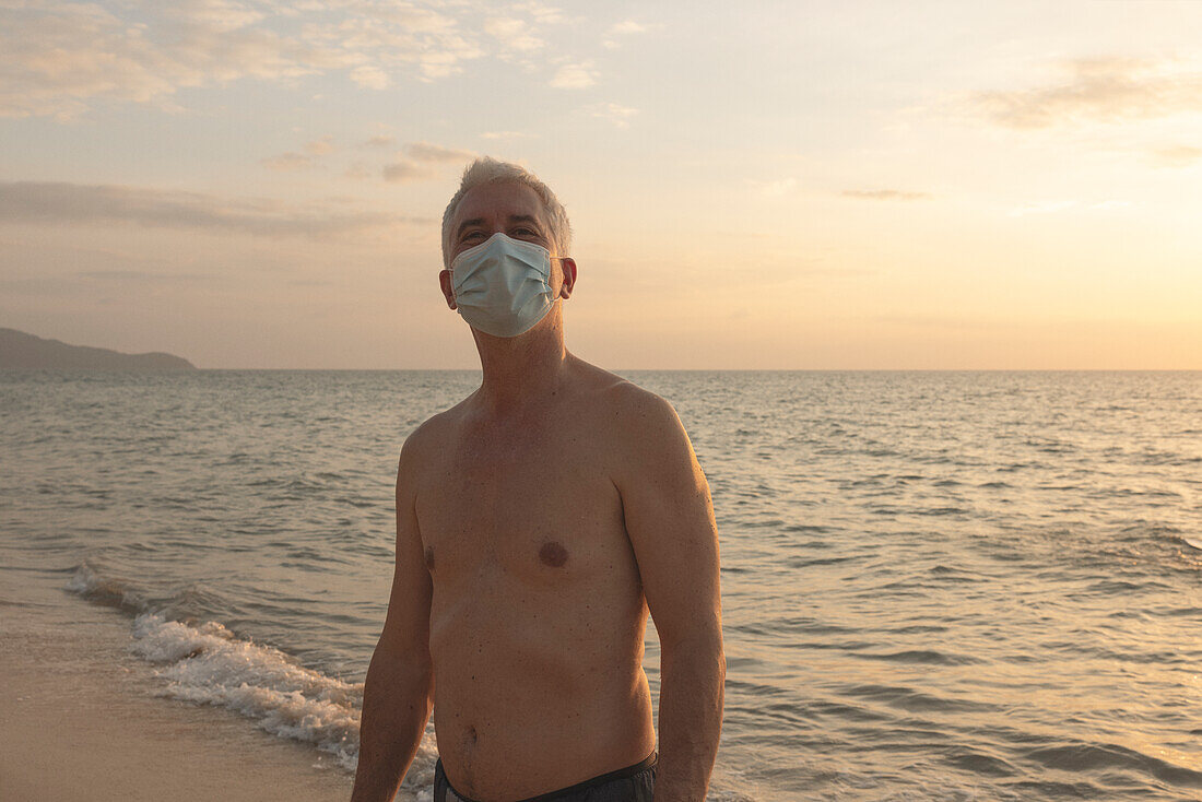 Senior man walking on beach in protective face mask