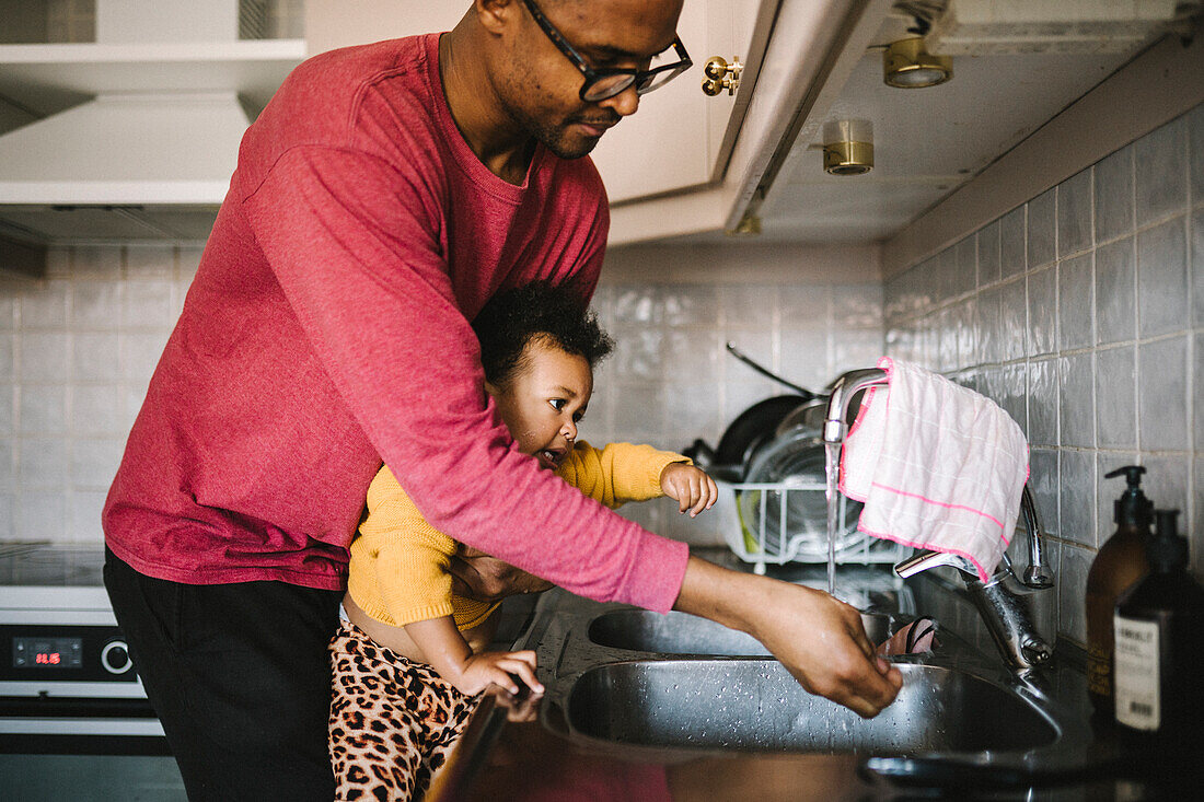 Father and daughter washing hands in kitchen sink