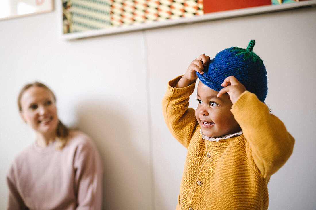 Mother looking at daughter putting on blue hat