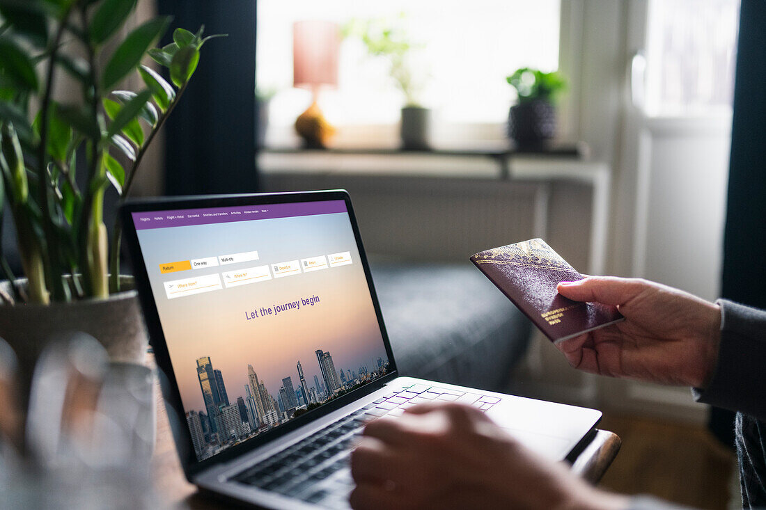 Man searching for flights on laptop and holding passport