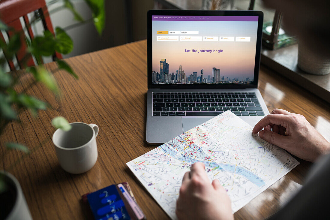 Man searching for flights on laptop and looking at map