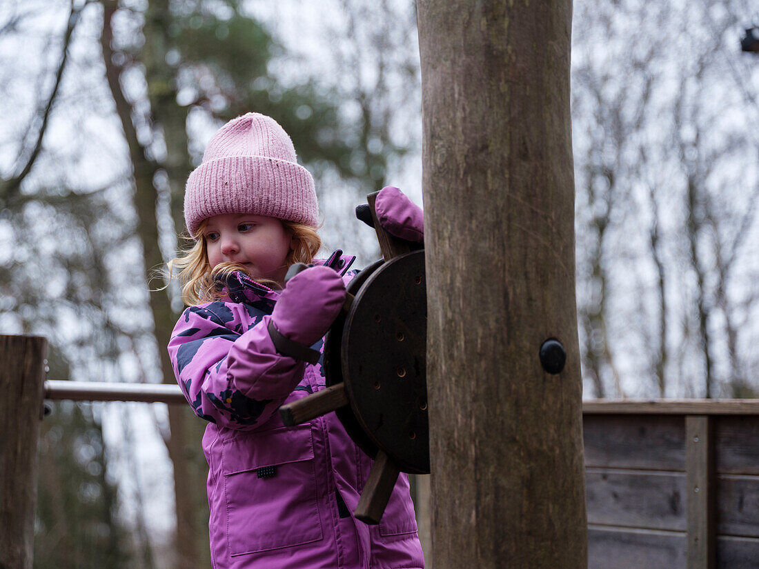 Girl in pink winter clothes holding rudder on playground