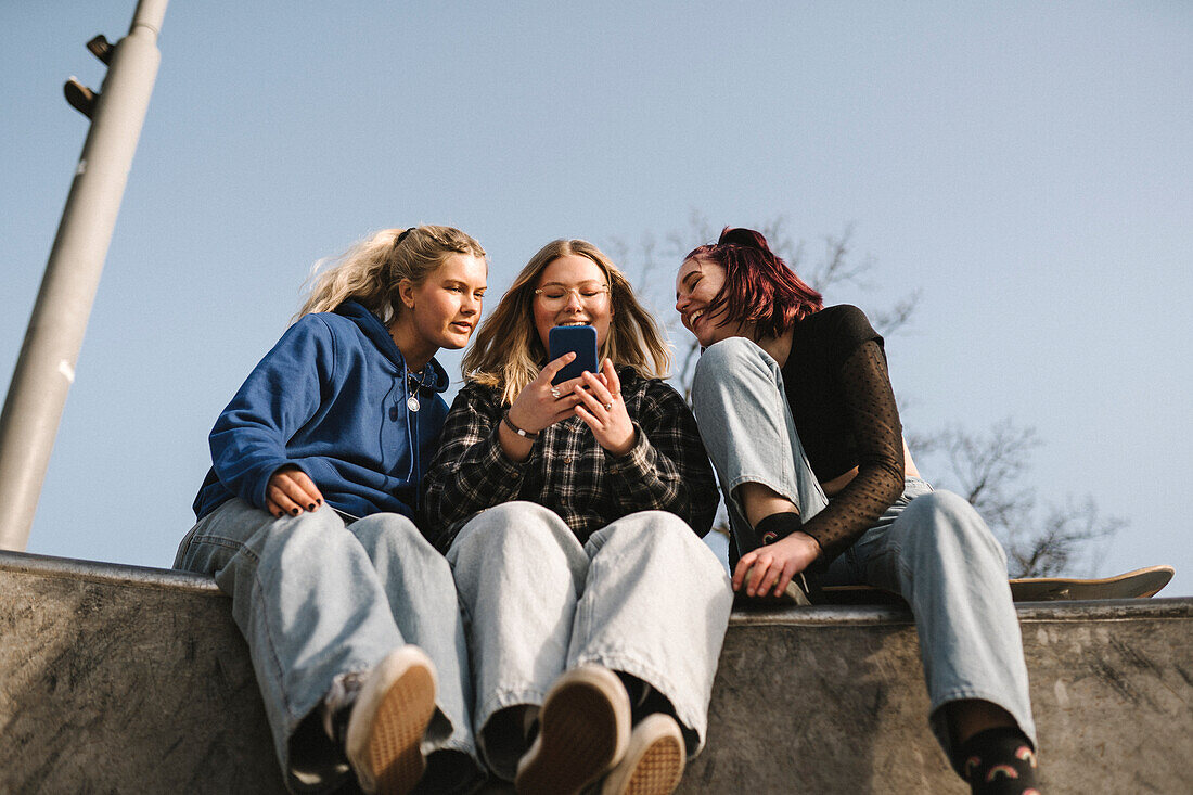 Lächelnde Teenager-Mädchen, die im Skatepark ein Smartphone benutzen