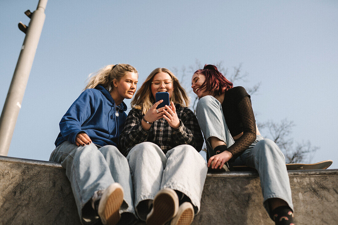Smiling teenage girls using smart phone in skatepark