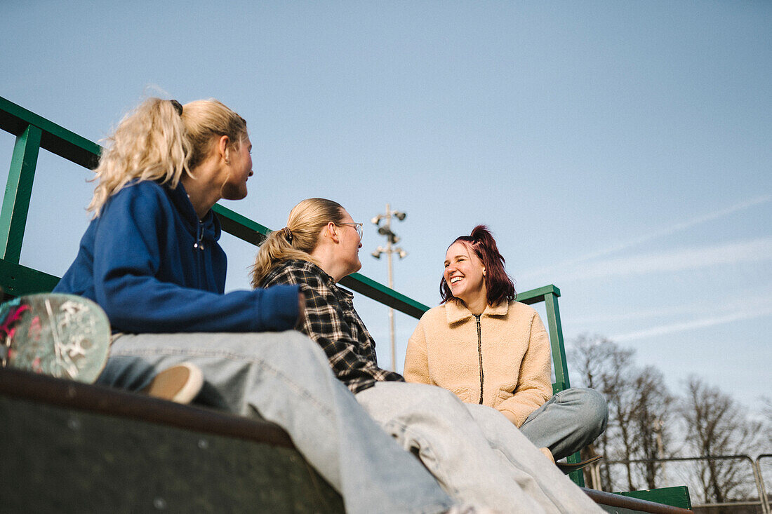 Lächelnde Teenager-Mädchen sitzen im Skatepark