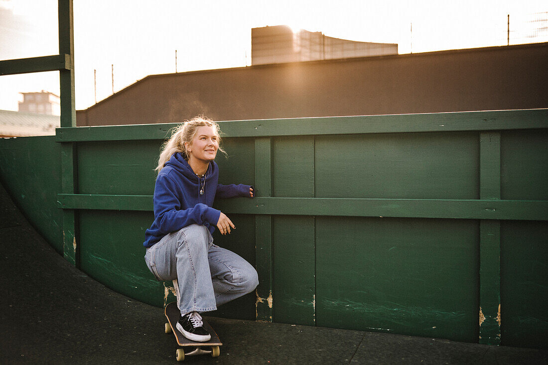 Smiling teenage girl crouching on skateboard