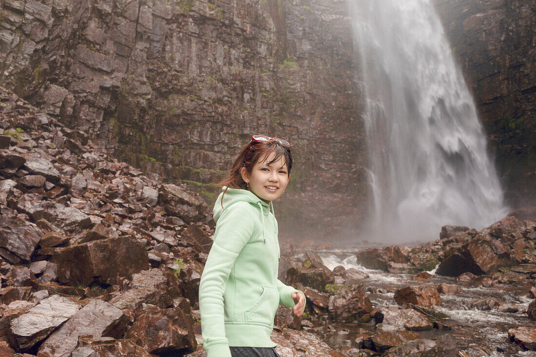 Lächelndes Mädchen steht vor einem Wasserfall