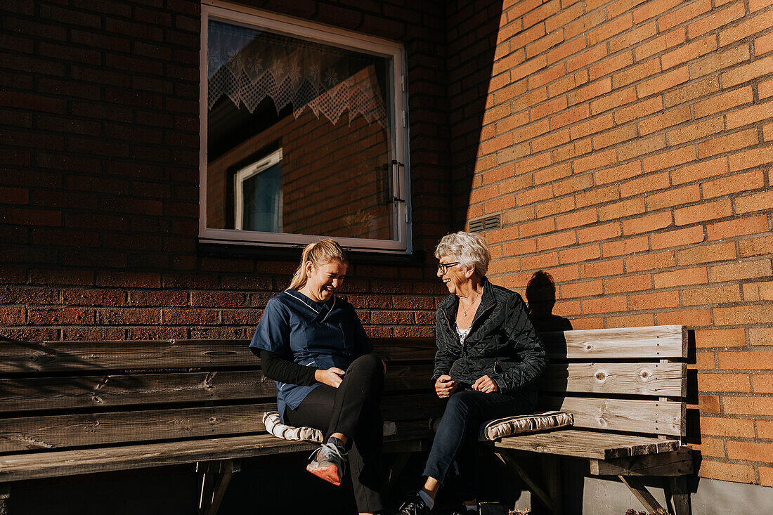 Home caretaker and senior woman sitting on bench and laughing