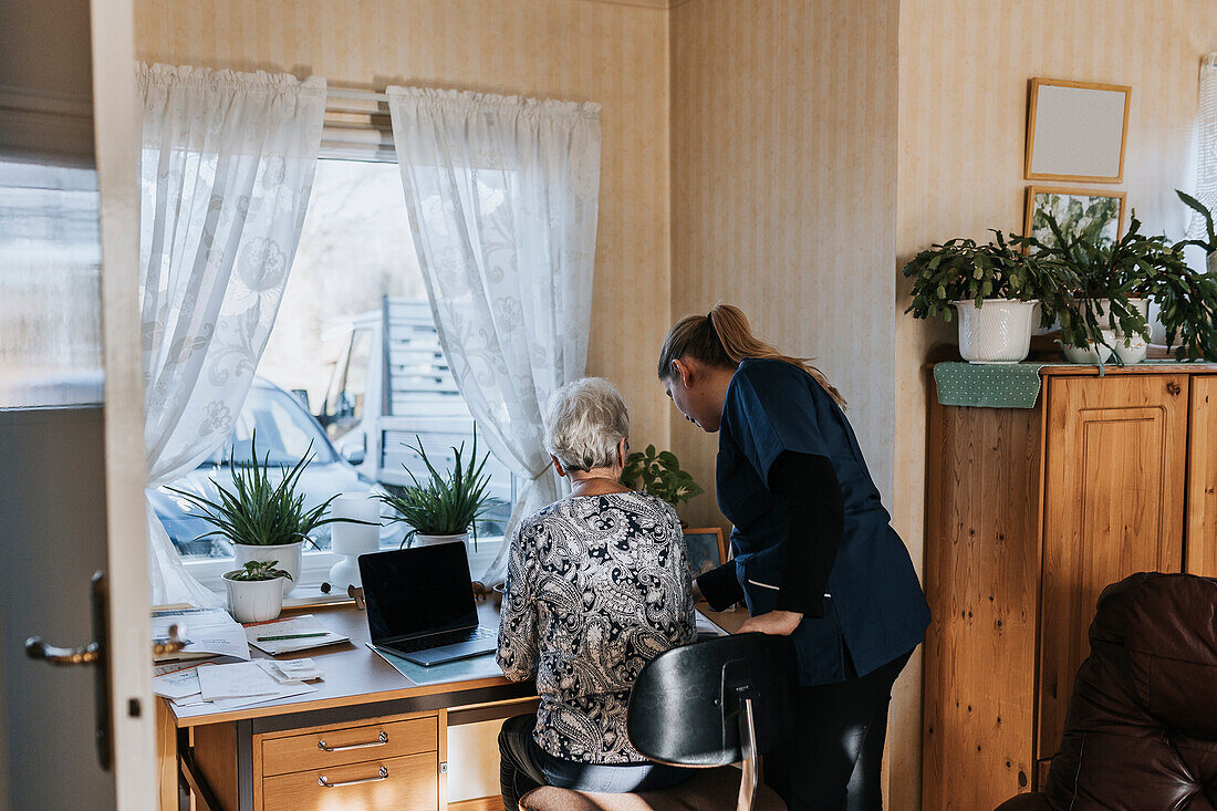 Hauspflegerin hilft Seniorin bei der Benutzung des Laptops