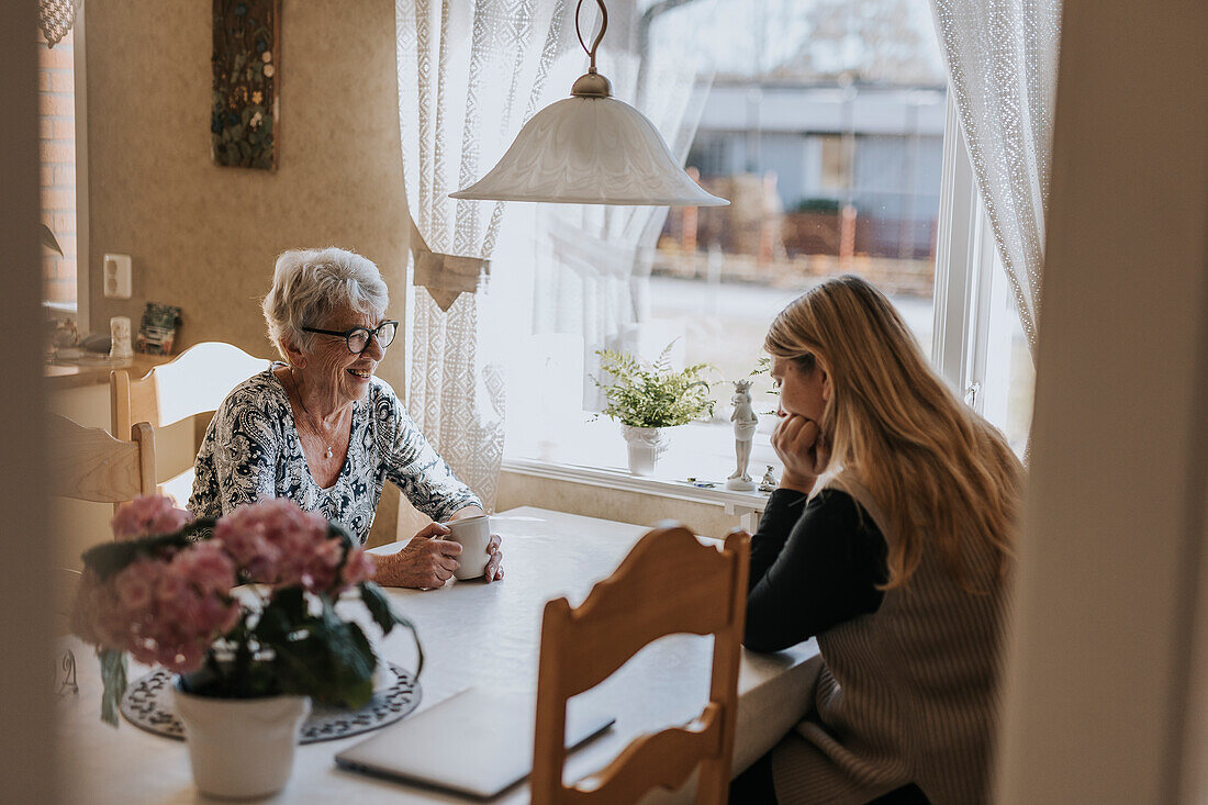 Grandmother and adult granddaughter sitting at table and having tea