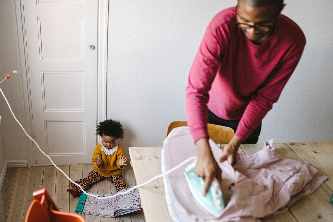 Father ironing clothes while daughter playing on floor