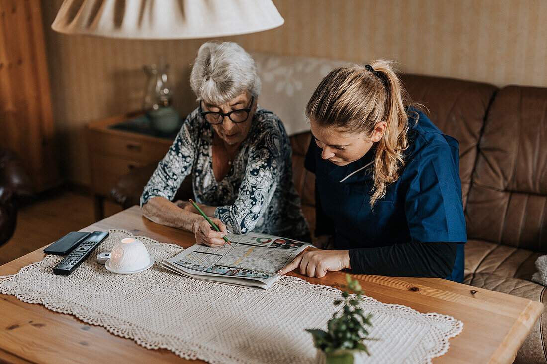 Hauspflegerin und Seniorin lösen Kreuzworträtsel